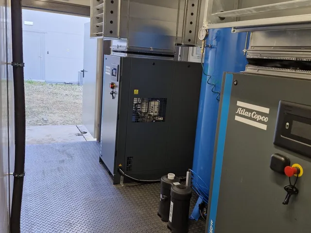 Wnętrze kontenera — sprężarka Atlas Copco, niebieski zbiornik buforowy i kratki wentylacyjne