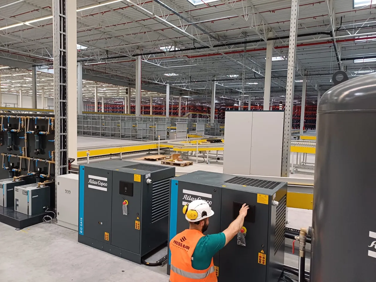 Serwisant Press Bar uruchamia sprężarkę śrubową Atlas Copco GA; obok druga sprężarka GA15, osuszacze ziębnicze F i panel filtrów sprężonego powietrza